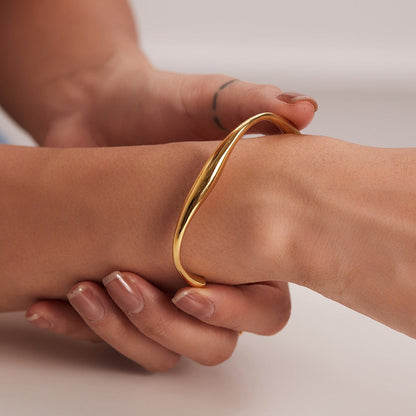 Gold bracelet on a wrist with a neutral background